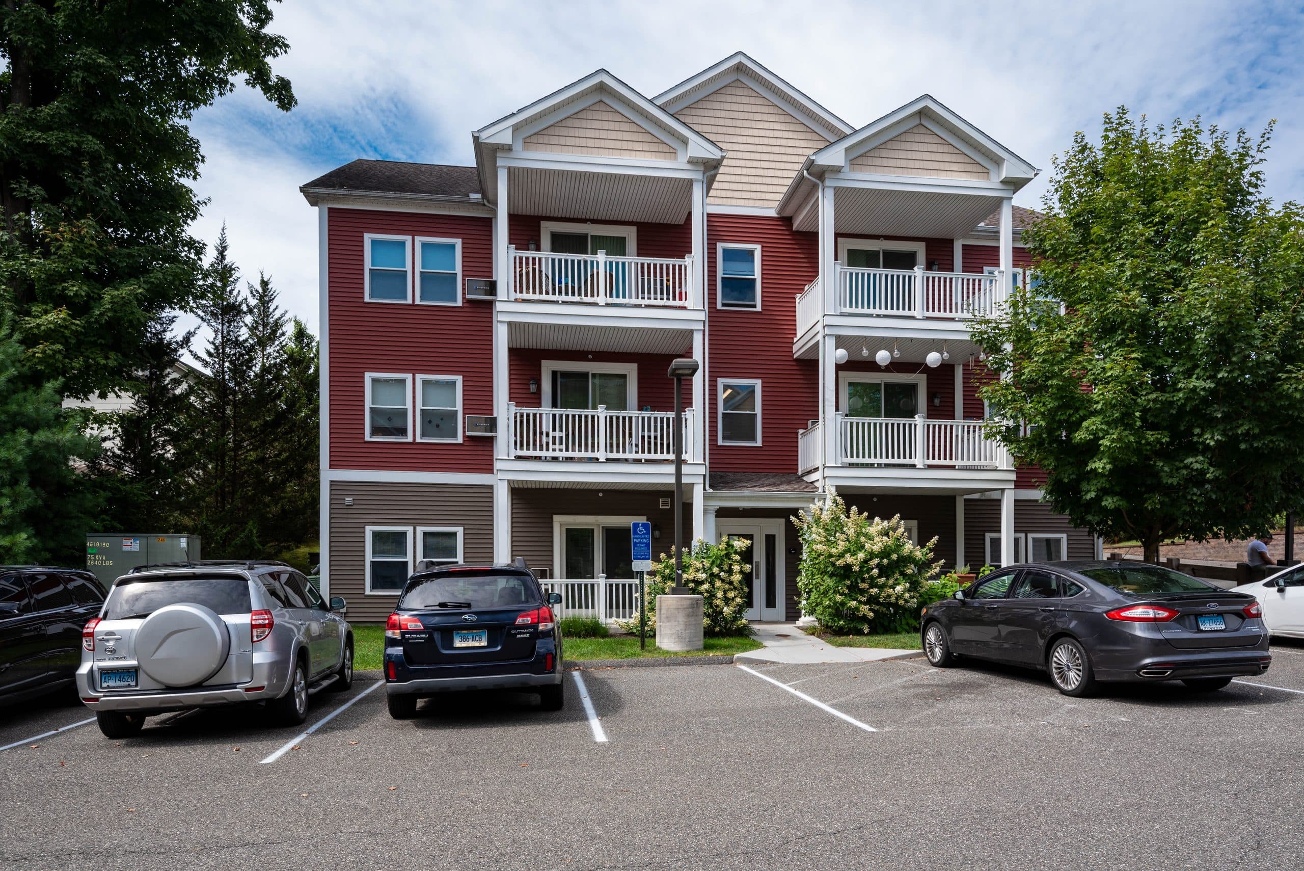 The front elevation of Barton Commons — three storeys of red clapboard with white gabled porches and private balconies, above the resident parking